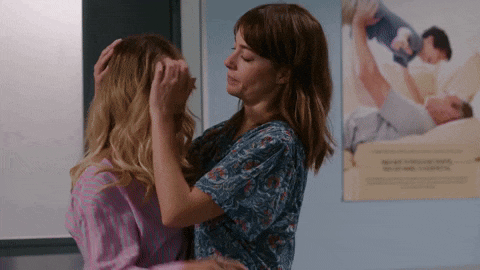 two women hugging in front of a poster of a man laying on a bed .