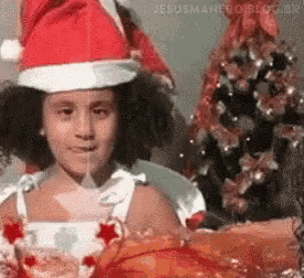 a little girl is wearing a santa hat and holding a christmas present .