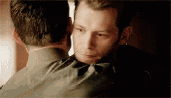 two men are hugging each other and one of them is looking at the other 's face .