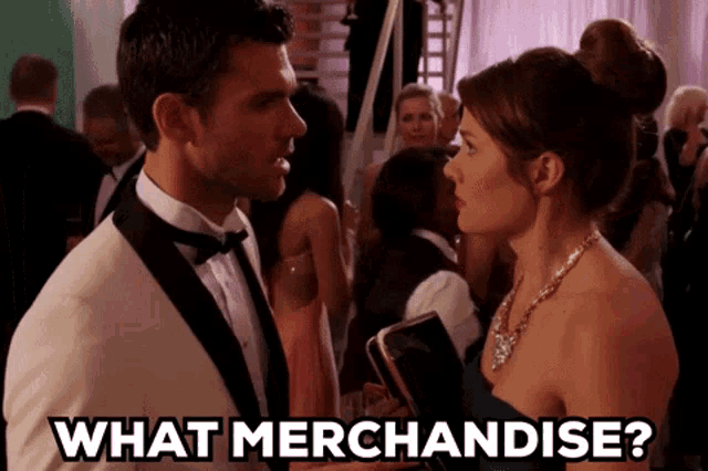 a man in a tuxedo is talking to a woman in a blue dress who is holding a book and asking what merchandise