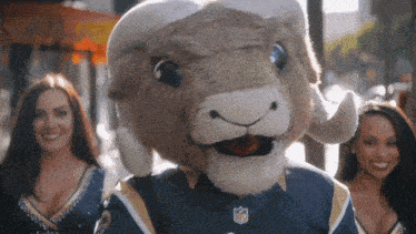 a ram mascot wearing a nfl jersey stands between two cheerleaders