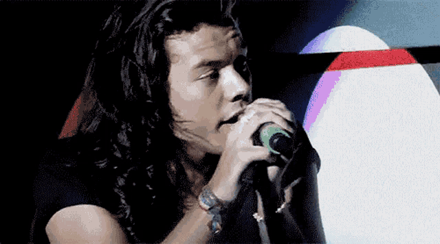 a man with long hair is singing into a green microphone .