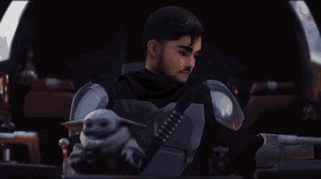 a man in armor holds a baby yoda in his lap