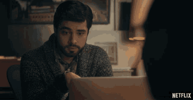 a man sitting at a desk looking at a laptop with a netflix logo in the corner