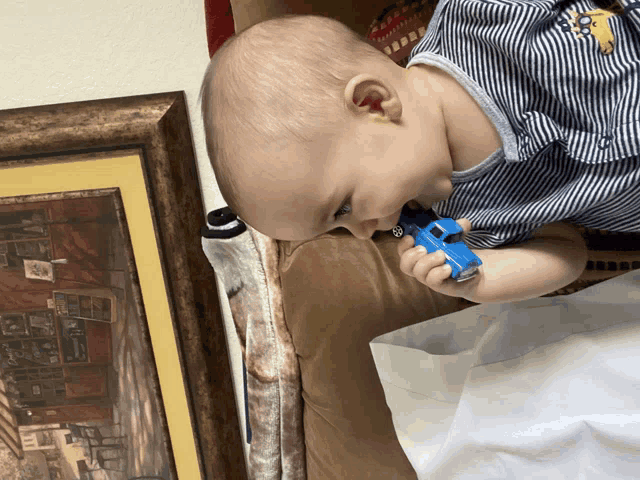 a baby in a striped shirt is playing with a blue toy car