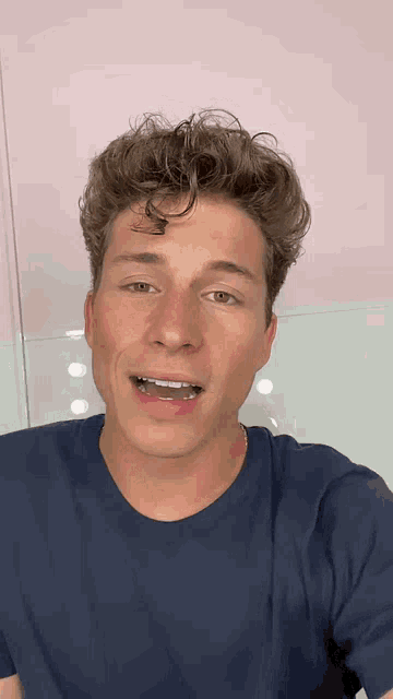 a man with curly hair is wearing a blue t-shirt