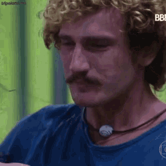 a close up of a man with curly hair and a mustache wearing a blue shirt