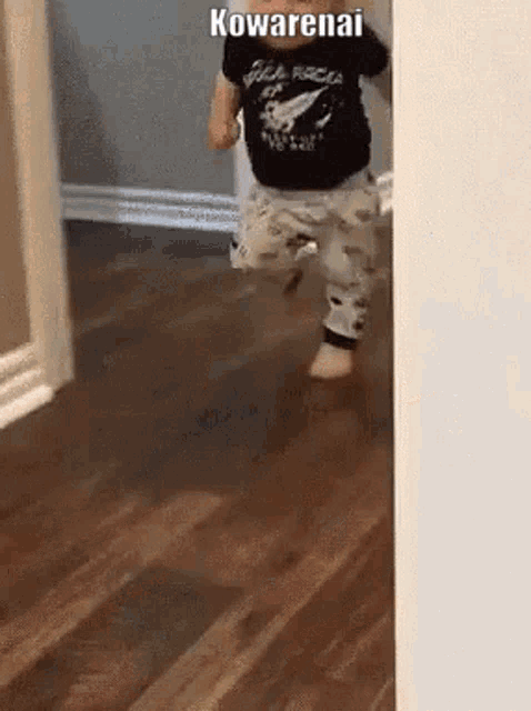a baby is running on a wooden floor in a room with the word kowarenai on the corner .