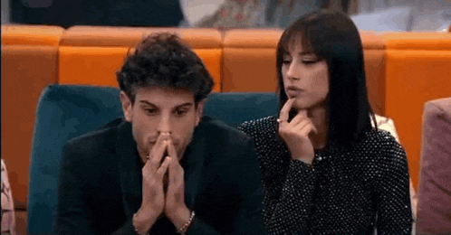 a man and a woman are sitting on a couch with their hands folded in prayer .