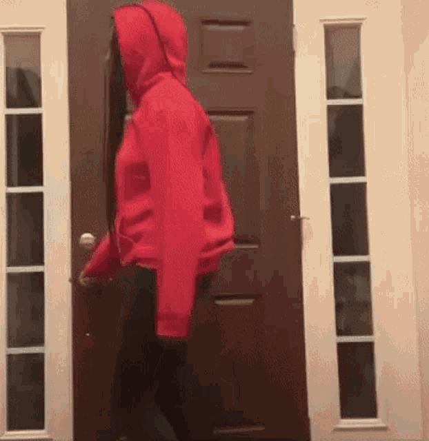 a woman in a red hoodie is walking through a door .