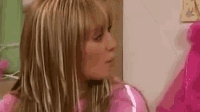 a woman with blonde hair and a pink shirt is standing in front of a pink balloon .