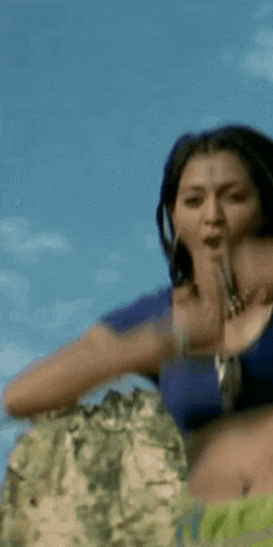 a woman wearing a blue crop top and a necklace is looking up at the sky .