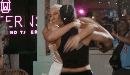 a man and a woman are hugging each other in front of a neon sign that says ' erin ' on it .