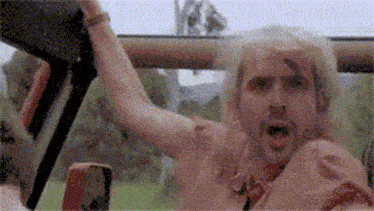 a man is sitting in a car with his arm in the air and his mouth open .
