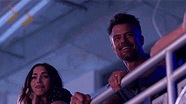 a man and a woman are standing next to each other on a balcony looking at something .