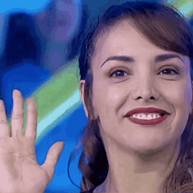 a woman with red lipstick is smiling and waving