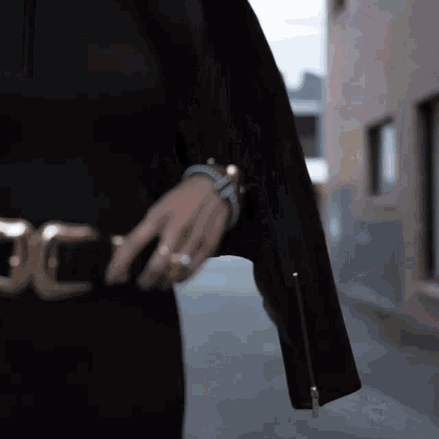 a woman wearing a black jacket and a gold belt is walking down a street