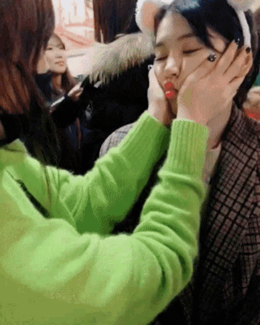 a woman in a green sweater is putting her hand on another woman 's face .