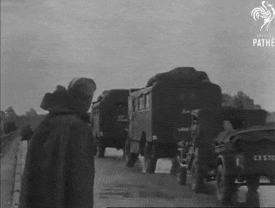 a black and white photo of a man standing next to a line of military vehicles