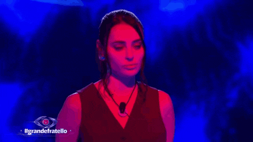 a woman in a red dress is standing in front of a blue background with the words grandefratello written on it .