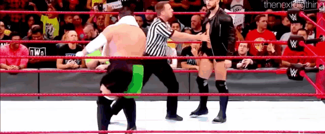 a referee is standing in the middle of a wrestling ring with two wrestlers .