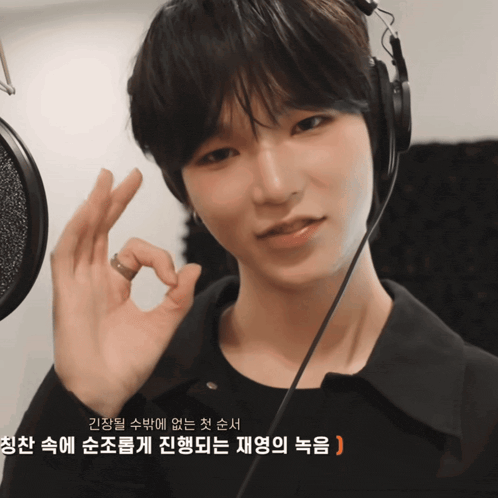 a young man wearing headphones and a black shirt is giving an ok sign