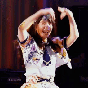 a woman is making a heart shape with her hands while dancing on a stage .