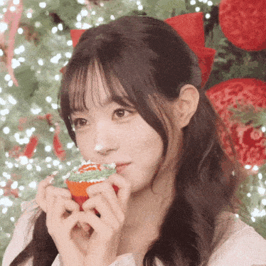 a girl with a red bow in her hair is holding a cupcake in front of her face