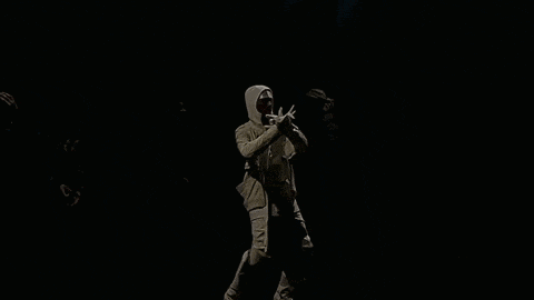 a man in a hooded jacket is standing in the dark .