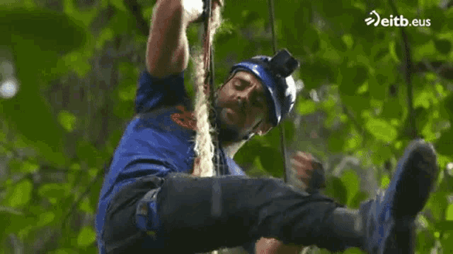 a man is climbing a tree with a rope and a helmet on .
