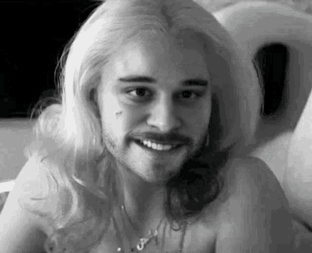a black and white photo of a man with long blonde hair and a beard smiling .