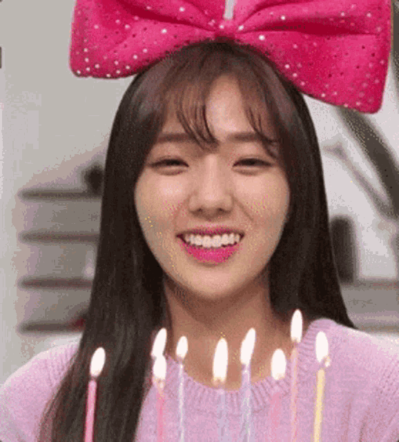 a woman with a pink bow on her head is smiling with candles around her neck