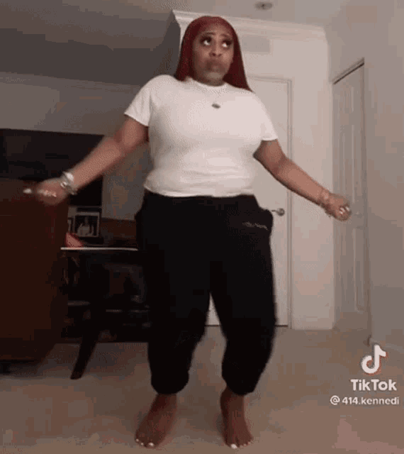 a woman is dancing barefoot in a living room wearing a white shirt and black pants .