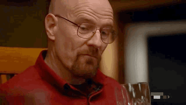 a bald man with glasses and a beard is sitting in a chair with a glass of wine .
