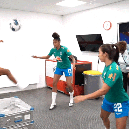 a woman in a green shirt with the number 13 on it stands next to another woman in blue shorts with the number 22 on them