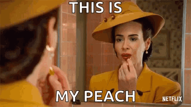 a woman is applying lipstick in front of a mirror while wearing a yellow hat .