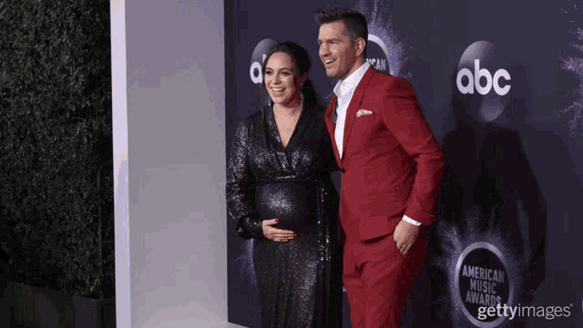 a man in a red suit stands next to a pregnant woman on a red carpet that says abc on it