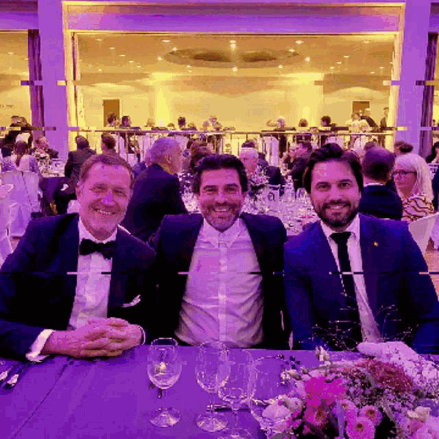 three men are posing for a picture at a table with wine glasses