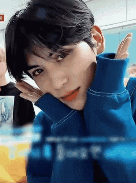 a close up of a person wearing a blue sweater with their hands on their face