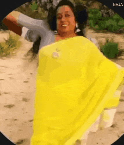 a woman in a yellow saree is dancing on a sandy beach