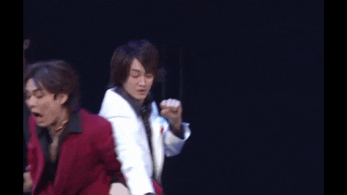 a man in a red jacket and a man in a white jacket are dancing on stage .