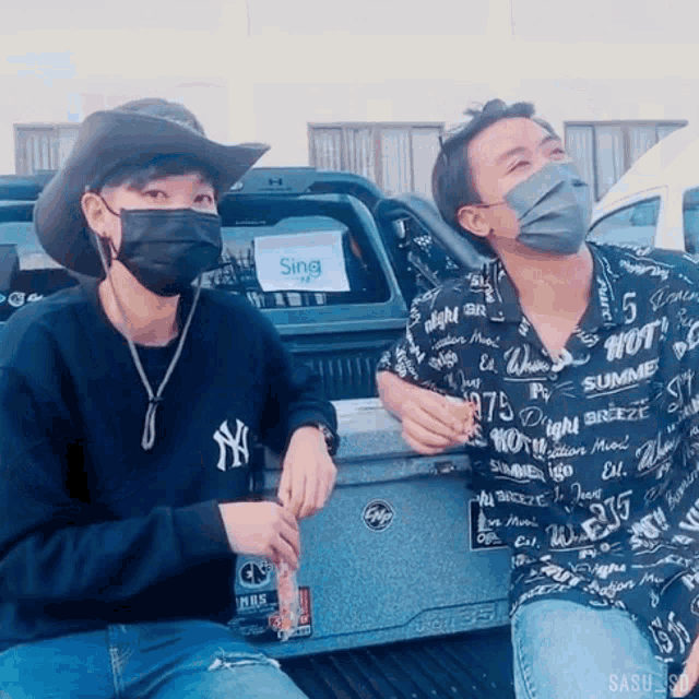 a man wearing a ny shirt sits next to another man wearing a black mask