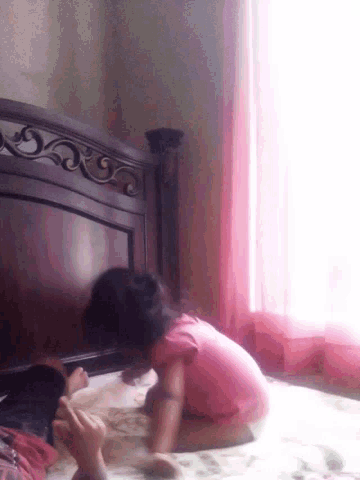 a woman in a pink shirt is sitting on a wooden dresser in front of a window