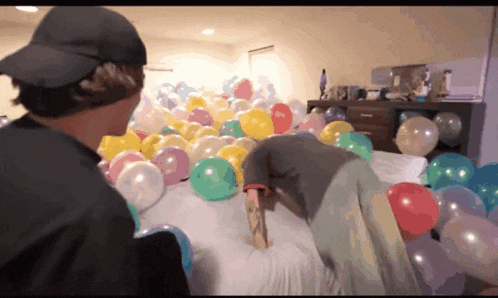 a person laying on a bed surrounded by balloons including one that says " i love you "
