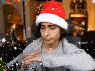 a man wearing a santa hat is sitting in front of a piano while snow is falling .