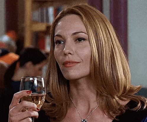 a woman is holding a glass of wine in her hand and smiling .