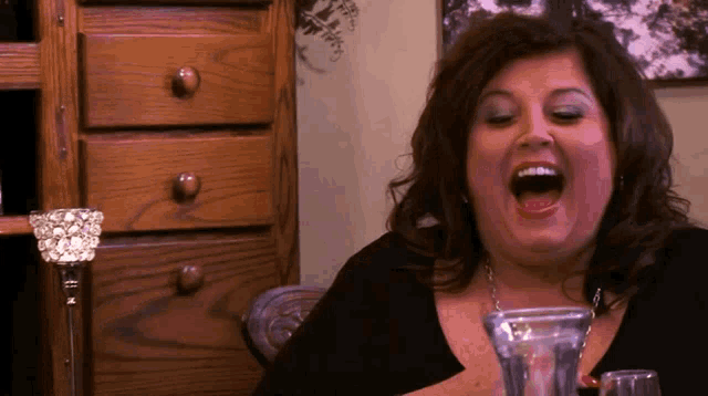 a woman is laughing while sitting at a table with a glass of wine in front of her