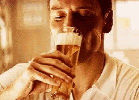 a man in a white shirt is drinking a glass of beer .