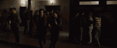 a man and a woman are walking through a crowd of people in a dark room .