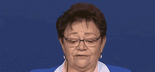 an elderly woman wearing glasses and a blue jacket looks at the camera